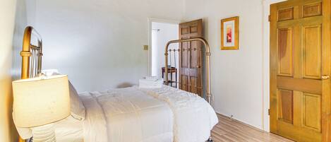 A bedroom with a bed, a bedside table with a lamp, a wooden door, and a framed picture on the wall.