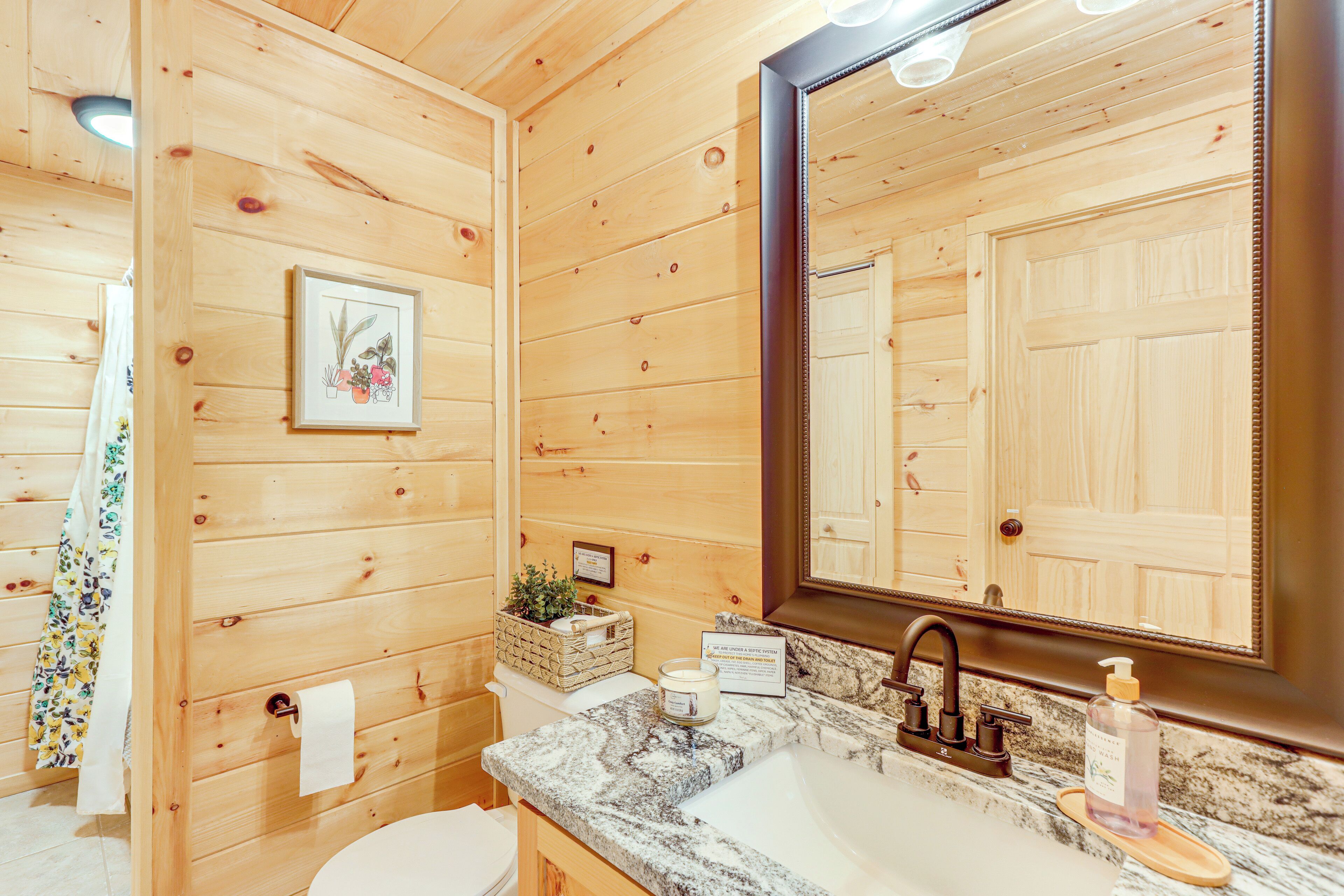 Une salle de bain rustique, avec des murs en bois, un lavabo en marbre, un grand miroir et une estampe botanique encadrée accrochée au mur.