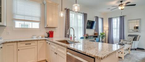 A modern kitchen with white cabinetry, granite countertops, a built-in dishwasher, and a central island.