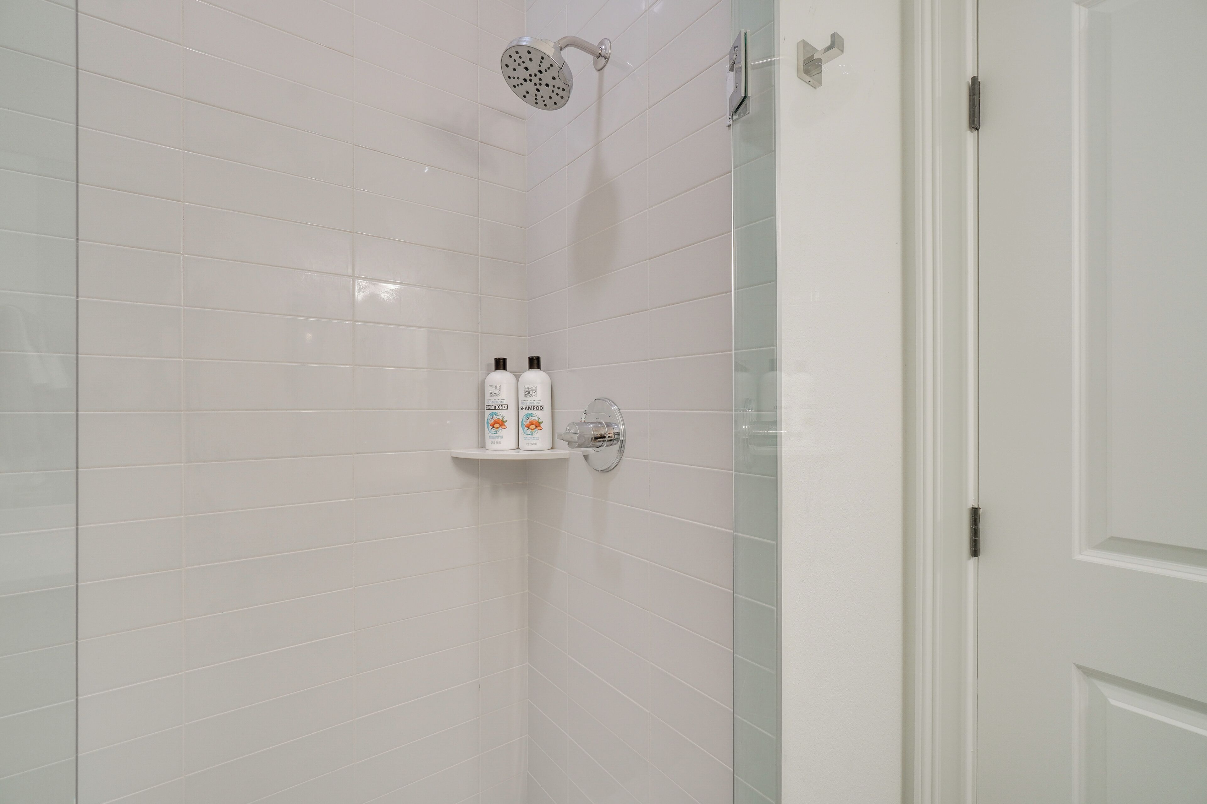 A bathroom with white tiled walls, a glass shower enclosure, and a white door.