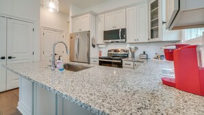 Una cocina con armarios blancos, encimeras de granito, electrodomésticos de acero inoxidable e iluminación colgante.