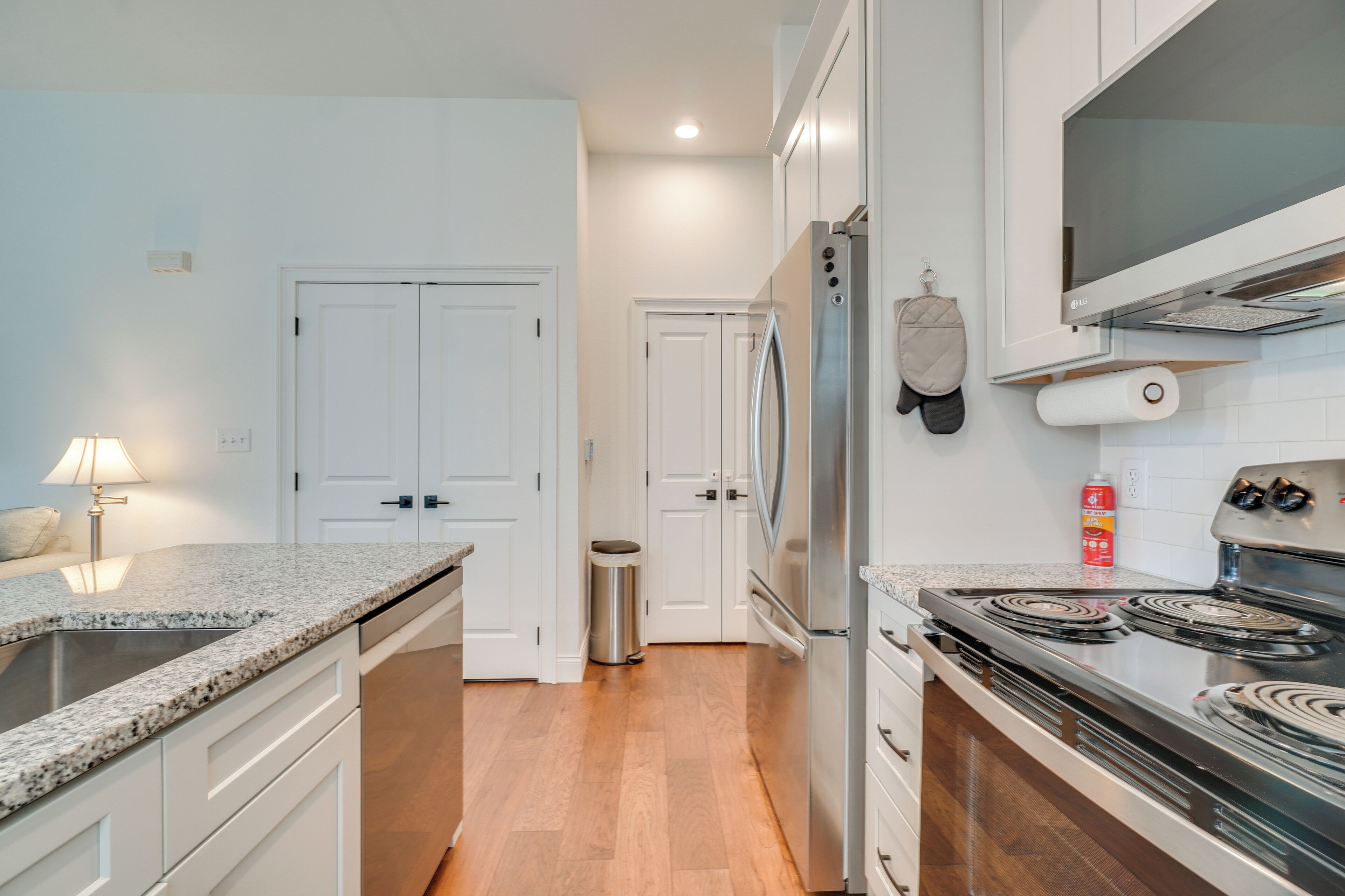 Una cocina moderna con armarios blancos, un refrigerador de acero inoxidable, una estufa y un microondas. Hay un bote de basura y un rollo de toallas de papel en la encimera.
