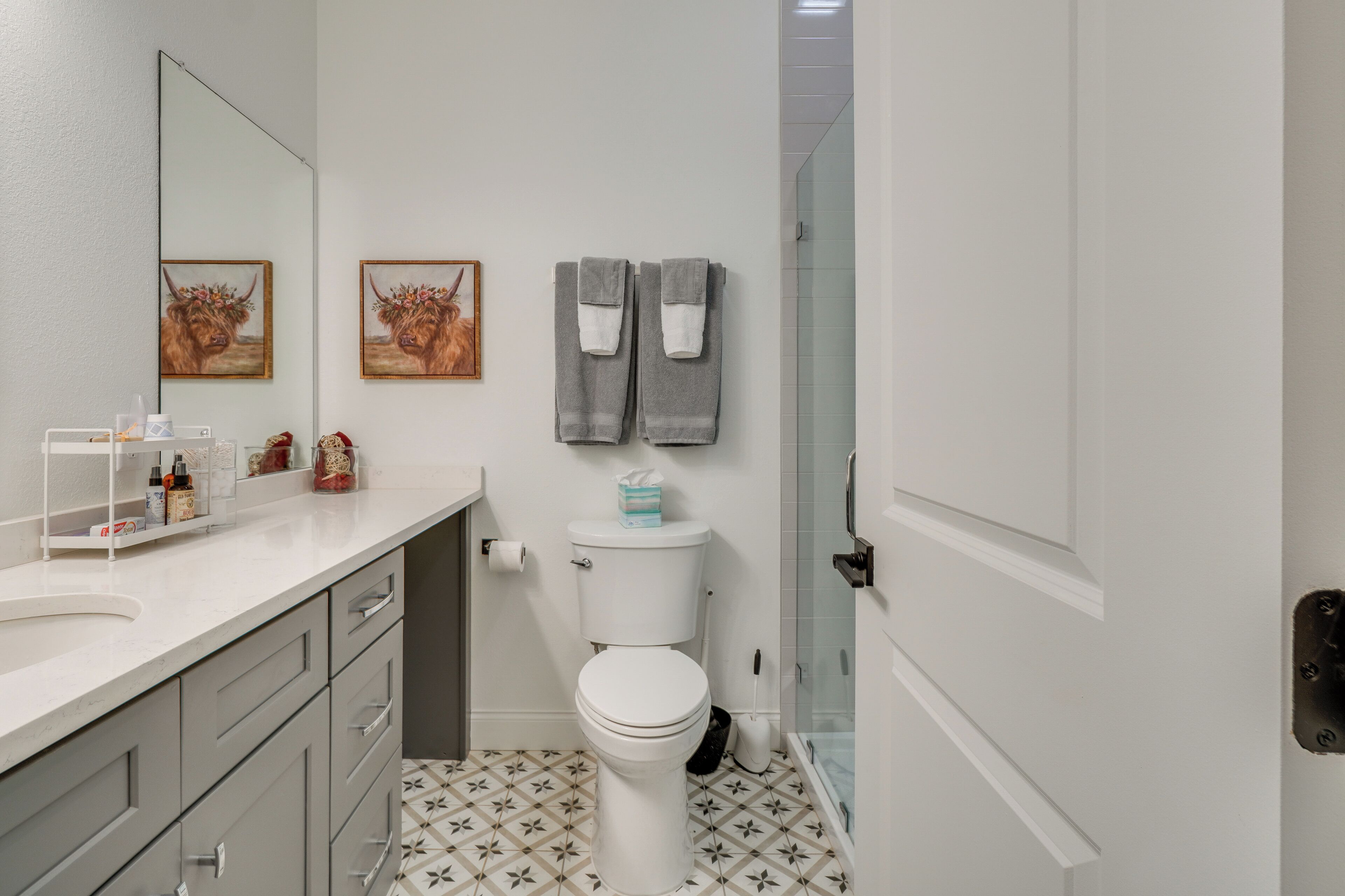 A bathroom with a white toilet, a sink with a mirror, and two towels hanging on the wall.
