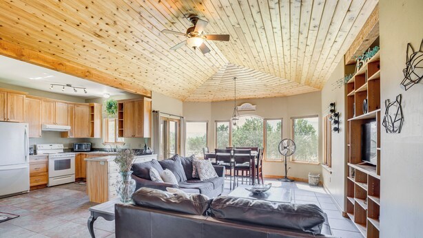 A modern kitchen with wooden cabinets, a dining area with a table and chairs, and a living room with a sofa. - Hunt, Fish & Explore: Mtn-view Home in Hotchkiss (Hotchkiss)