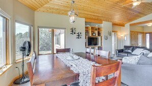 A dining area with a wooden table, chairs, and a fan. There is a ceiling fan, a fireplace, and a sofa in the background. - Hunt, Fish & Explore: Mtn-view Home in Hotchkiss (Hotchkiss)