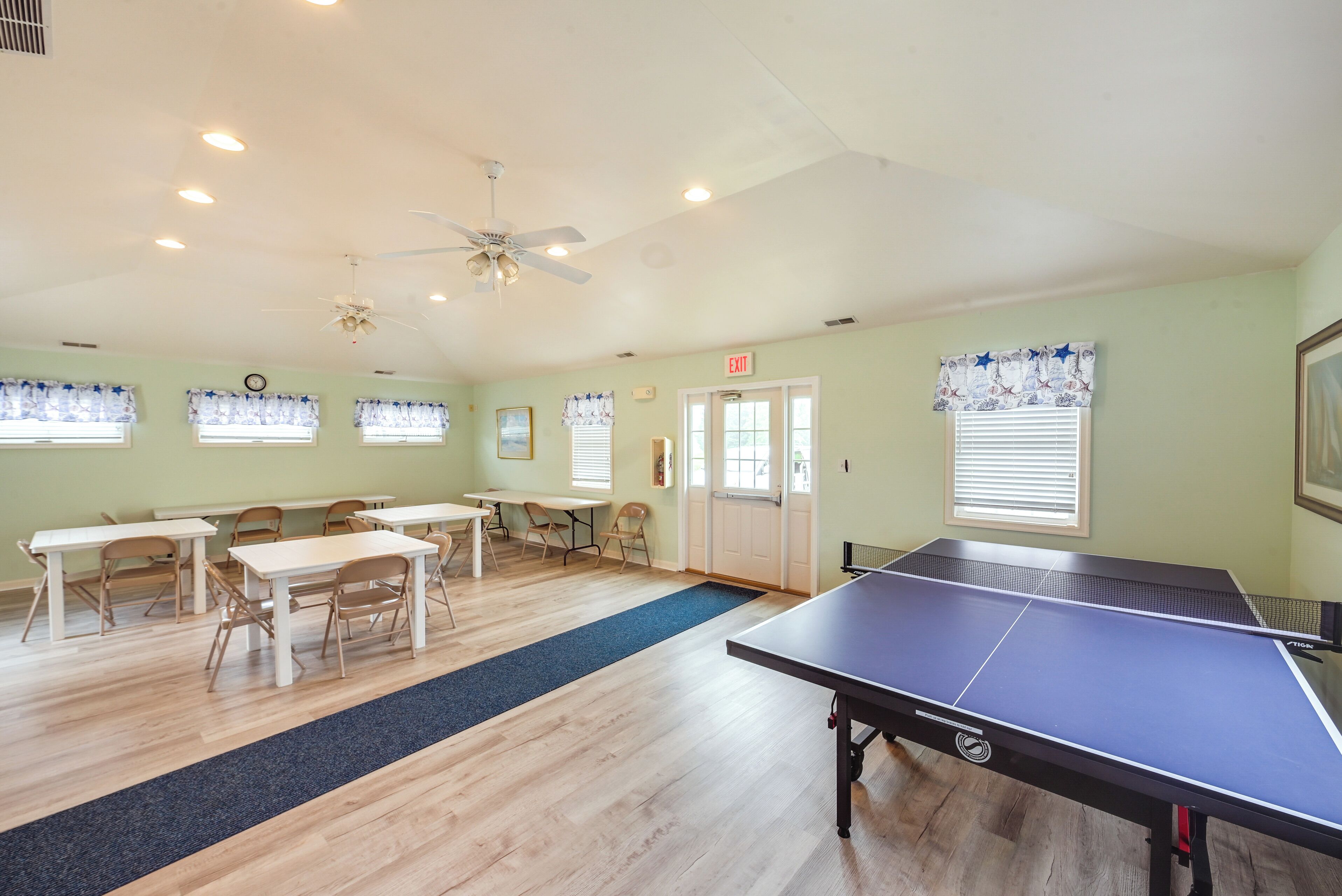 Une pièce équipée d’une table de ping-pong, de plusieurs tables, de chaises et d’un ventilateur de plafond.
