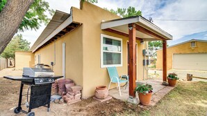 Une petite maison avec un patio, un barbecue et des plantes en pot.