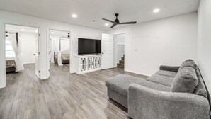 A spacious living room with a gray sofa, a flat-screen TV on a cabinet, and a ceiling fan.