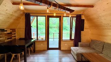 Un accogliente chalet in legno con tavolo, sedie, divano e ampie finestre che si affacciano sul paesaggio.