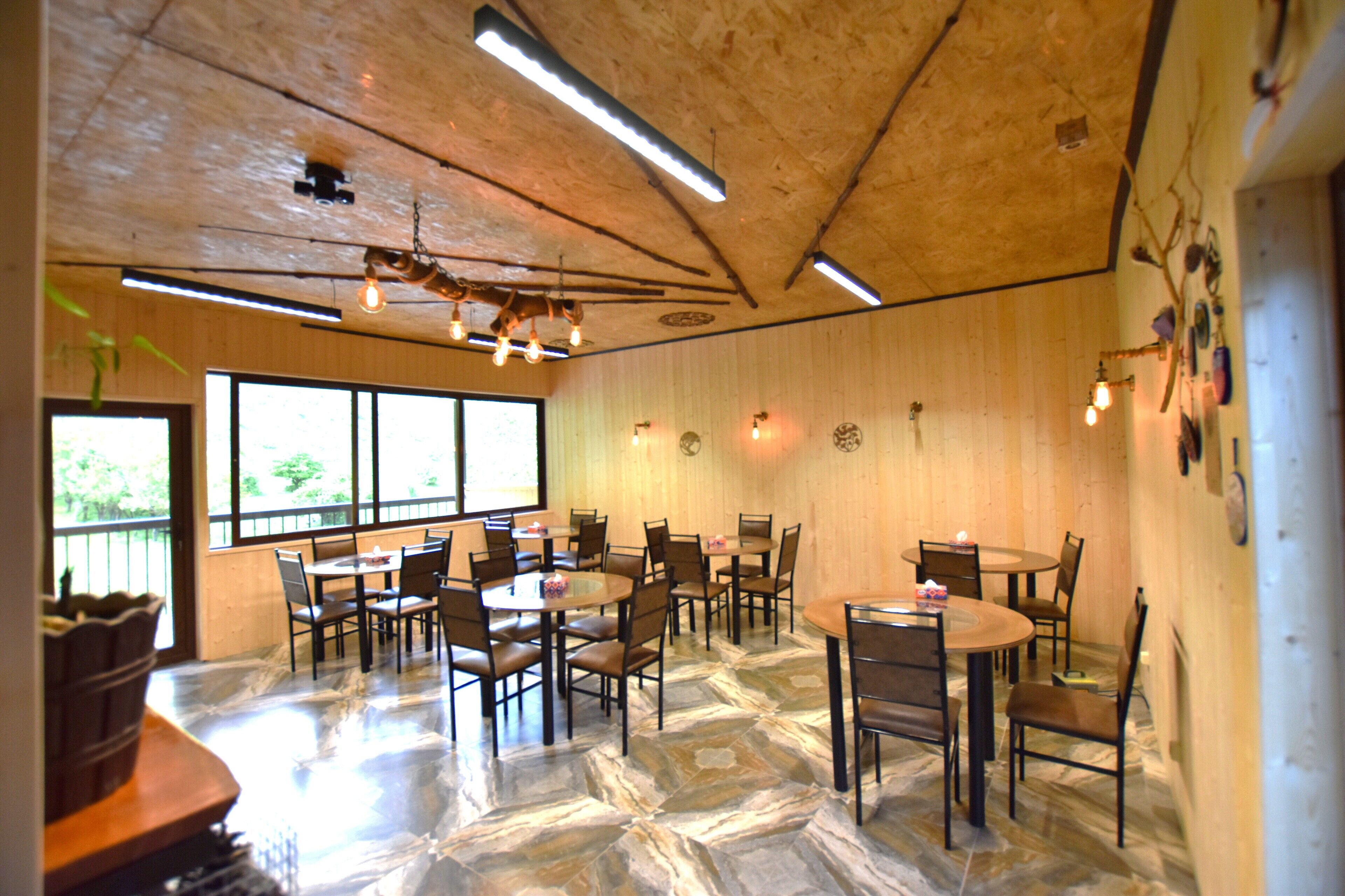 Um restaurante com várias mesas e cadeiras, paredes de madeira e um chão com padrão de pedra.