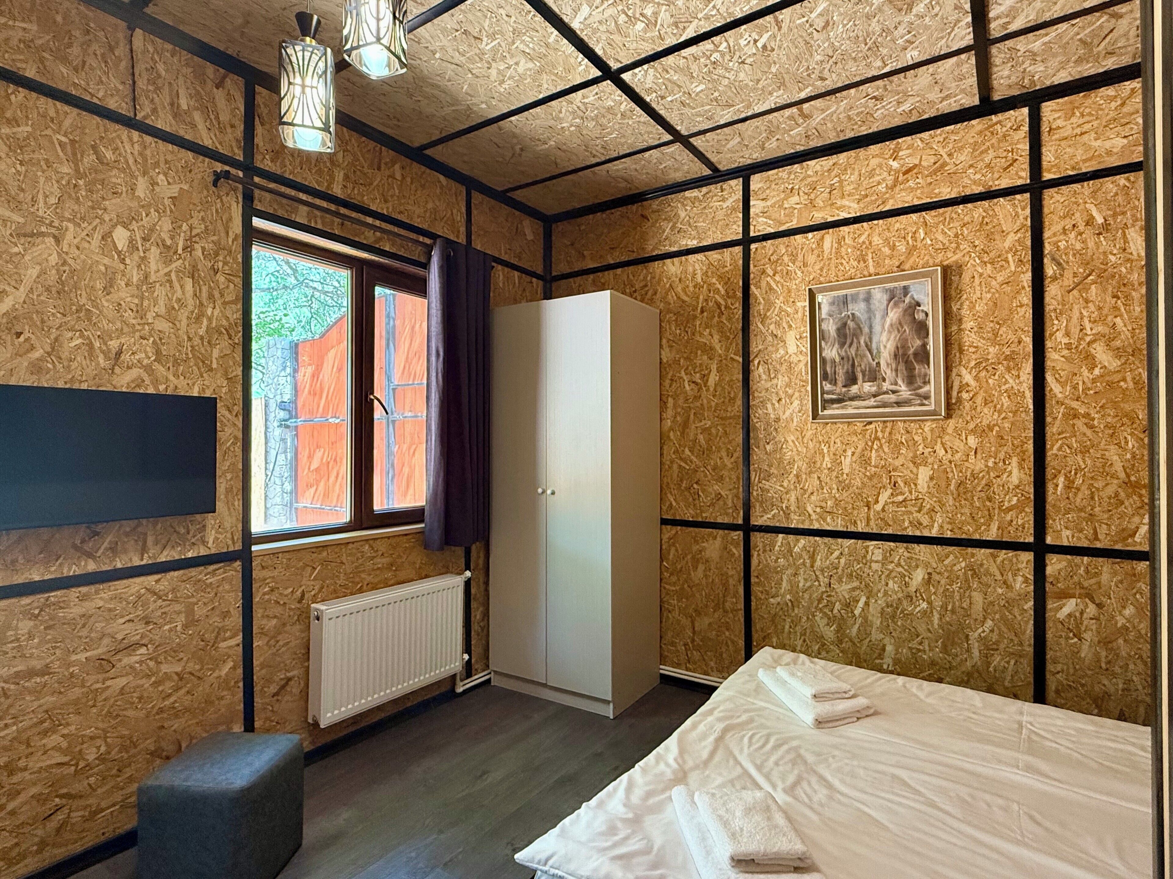 A room with a bed, a wardrobe, a radiator, a window with curtains, and a framed picture on the wall.