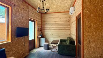 Interior de una cabaña con detalles de madera, un televisor montado en la pared, un sofá verde, una mesita y un accesorio de iluminación en el techo.