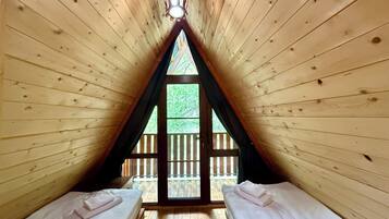 Habitación con paredes de madera y techo inclinado, con dos camas y una ventana que da a una terraza de madera.