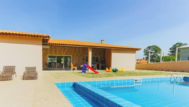 A swimming pool with a slide, two wicker chairs, and a brick building with a tiled roof.