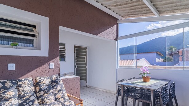 A balcony with a table and chairs, a potted plant, and a view of a mountain and buildings. - Apartamento em Ubatuba com Churrasqueira (Ubatuba)