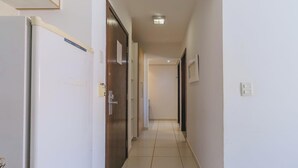 A narrow hallway with white walls and a tiled floor, leading to a door at the end.