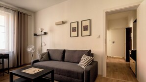 Un soggiorno moderno con un divano grigio, un tavolino da caffè nero e una ventola. Si notano due quadri appesi alla parete, una lampada e un pavimento in legno.