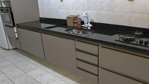 Cozinha com bancada preta, eletrodomésticos de aço inoxidável e painel de azulejos brancos.
