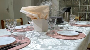 Uma mesa de jantar posta com jogos americanos cor-de-rosa, copos de vidro transparente e um centro de mesa branco.
