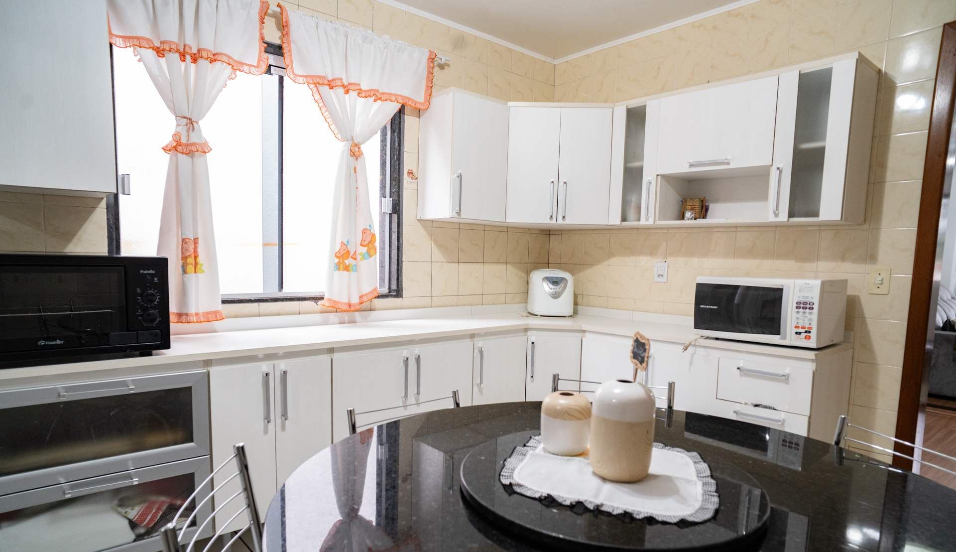 Una cocina con armarios blancos, microondas, tostadora y cafetera.