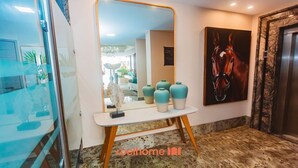 A hotel lobby with a large mirror, a horse painting, and a reception desk with vases.
