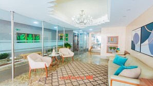 A modern lobby with a chandelier, seating area, and a reception desk.