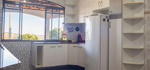 Una cocina con ventana, armarios blancos, un refrigerador y una botella de licor.