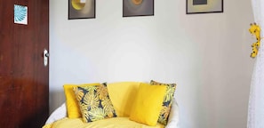 Una habitación con un sofá amarillo, una puerta de madera y tres obras de arte enmarcadas en la pared.