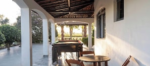 Una mesa de billar con sillas, una pérgola y vistas a árboles y una valla.