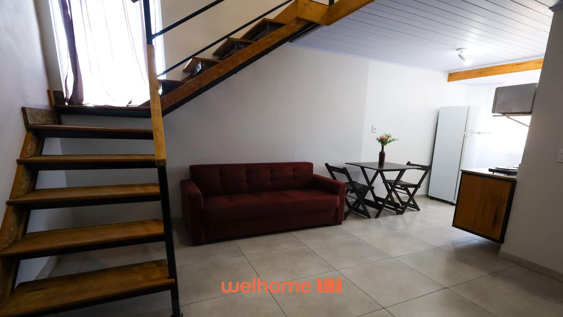 A staircase leading to a loft bedroom, a red sofa, a dining table with chairs, and a kitchen area.
