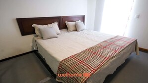 Een net opgemaakt bed met een houten hoofdbord, een beige deken en een geborduurde plaid.