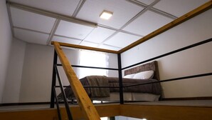 Una habitación con literas, una escalera de madera y una ventana con cortinas.