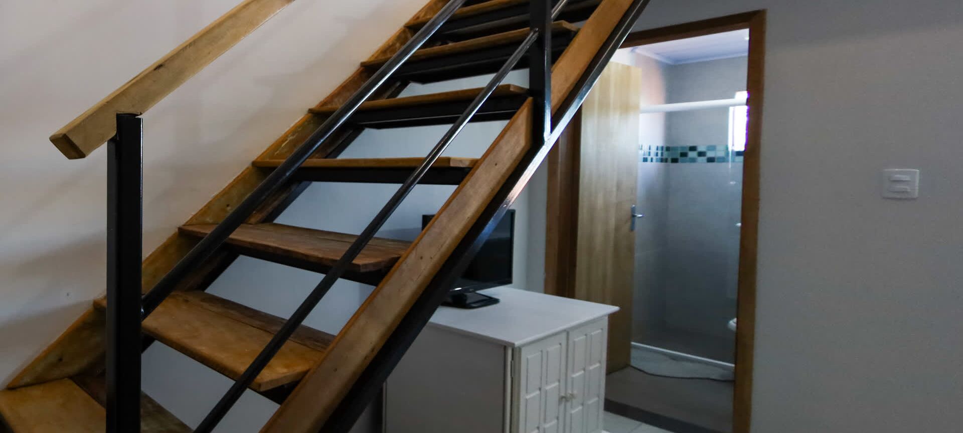 A staircase with wooden steps and metal railings, leading to a room with a white cabinet and a door leading to another room.