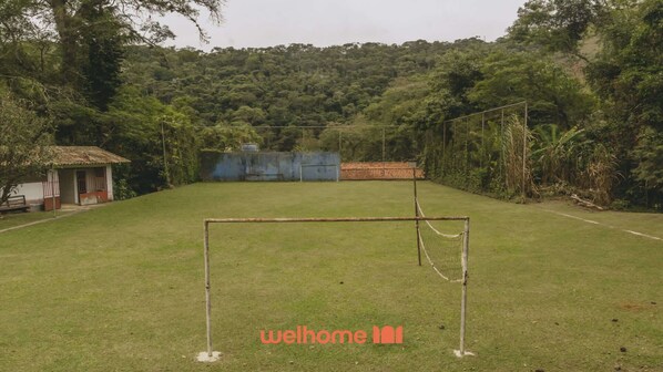 Un campo cubierto de hierba con un arco de fútbol, un edificio pequeño y un bosque denso al fondo.