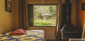 A bedroom with a bed, a window with a view of greenery, and a TV.