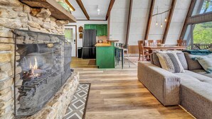 A cozy interior with a stone fireplace, wooden beams, a green kitchen island, and a comfortable seating area. - Press Pause | Hot Tub + Epic Mountain Views (Beech Mountain)
