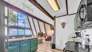A kitchen with wooden floors, a stone column, and a large window overlooking a scenic view. - Press Pause | Hot Tub + Epic Mountain Views (Beech Mountain)
