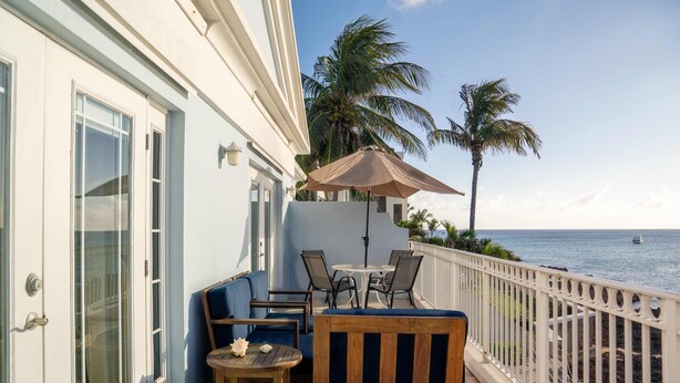 Un balcon avec une table et des chaises, un banc en bois et une vue sur l’océan.