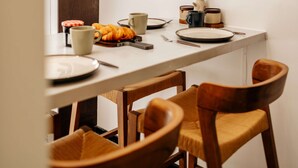 A dining area with a white table, wooden chairs, and a framed picture of fruit on the wall. - The Primrose Mews in Greater London (London)