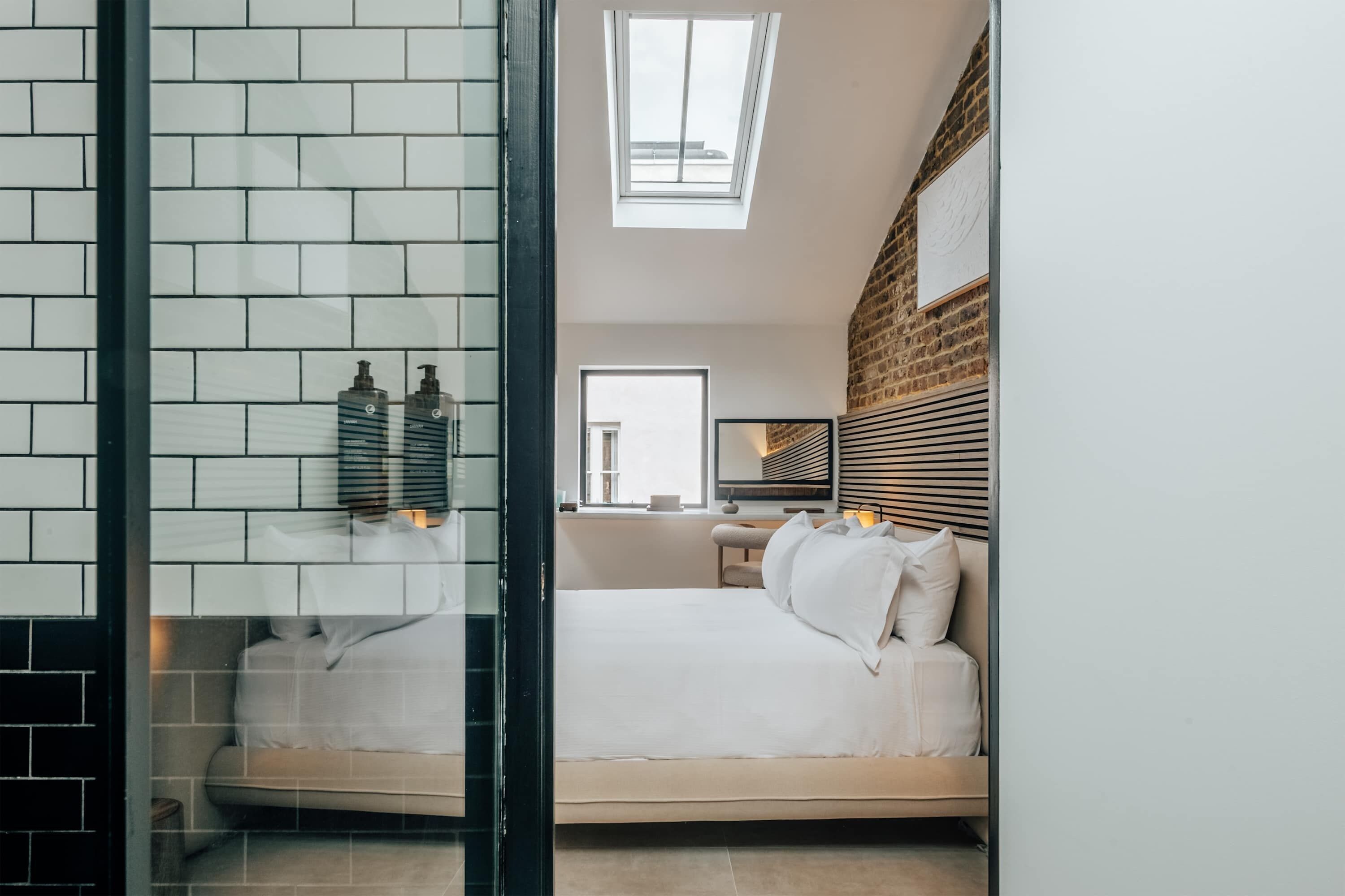 A modern bedroom with a skylight, a bed with white bedding, a brick wall, and a wooden headboard.
