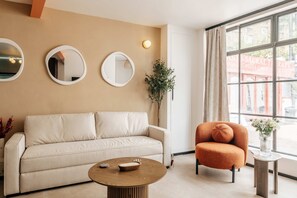 A modern living room with a beige sofa, a round coffee table, and a vibrant orange armchair. - The Primrose Mews in Greater London (London)
