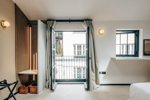 A modern hotel room with a sliding door leading to a balcony, a bed, a small table, and a wall-mounted shelf.