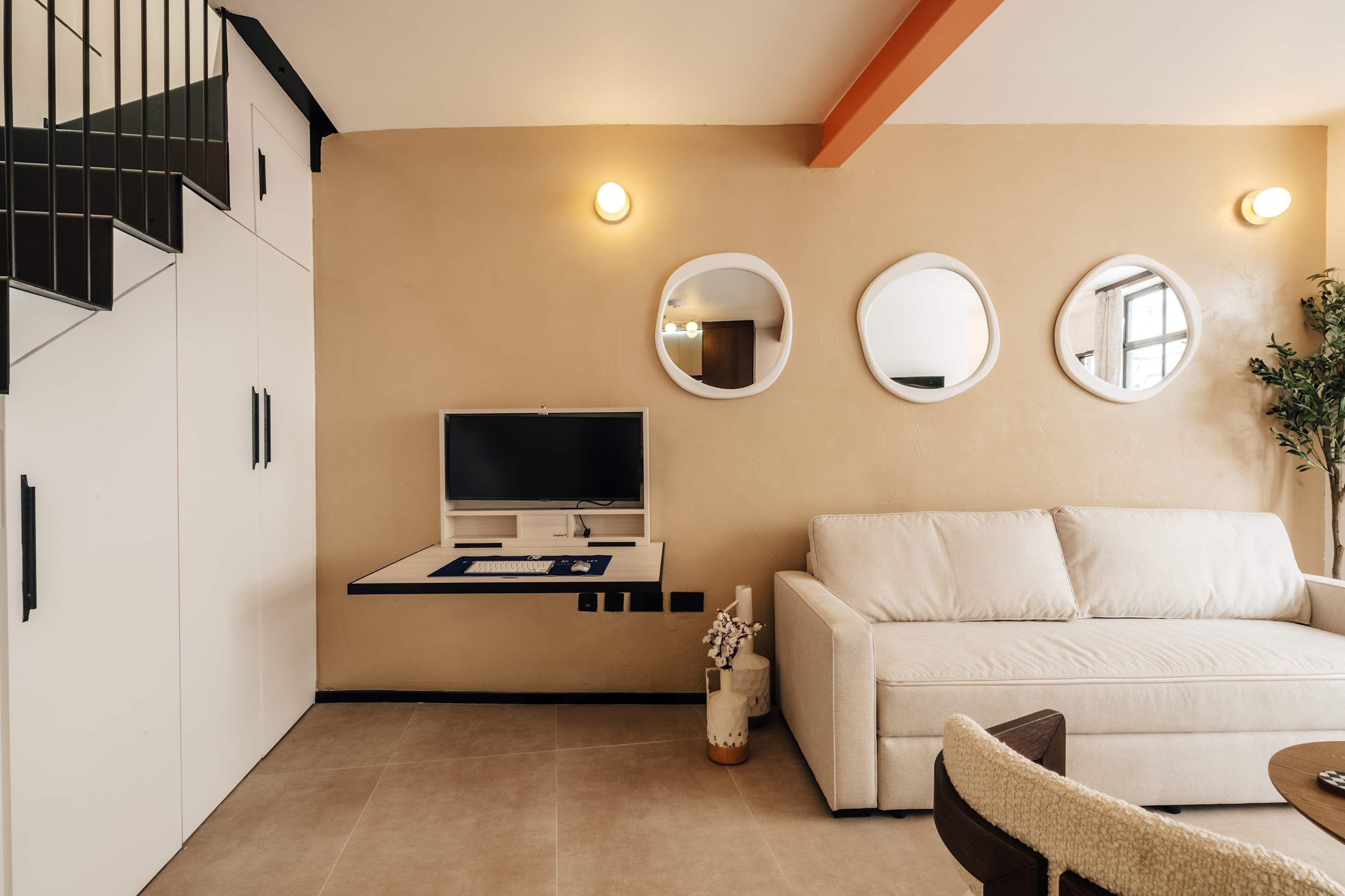 A modern living room with a sofa, a TV mounted on a wall, and a staircase.
