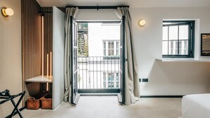 Moderni hotellihuone, jossa on liukuovi, joka johtaa parvekkeelle. Huoneessa on sänky, pieni pöytä ja seinälle kiinnitetty hylly.