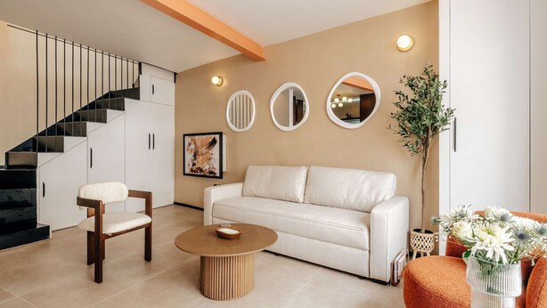 A modern living room with a staircase, white sofa, round coffee table, and decorative mirrors. - The Primrose Mews in Greater London (London)