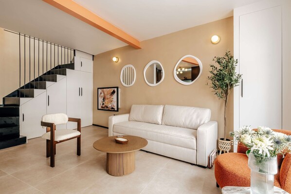 A modern living room with a staircase, white sofa, round coffee table, and decorative mirrors. - The Primrose Mews in Greater London (London)