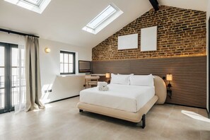A modern bedroom with a large bed, skylights, a brick wall, and a wooden headboard. - The Primrose Mews in Greater London (London)
