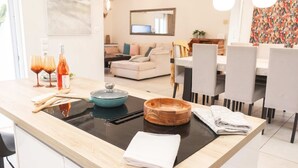 Une cuisine moderne avec un îlot central, un coin repas avec des chaises et un salon à l’arrière-plan.