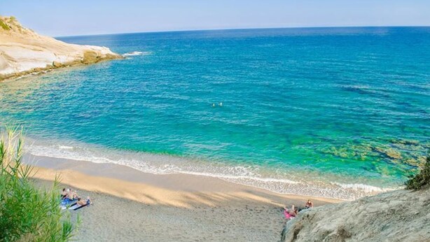 Une plage à l’eau turquoise et limpide, avec un rivage sablonneux et des falaises rocheuses.