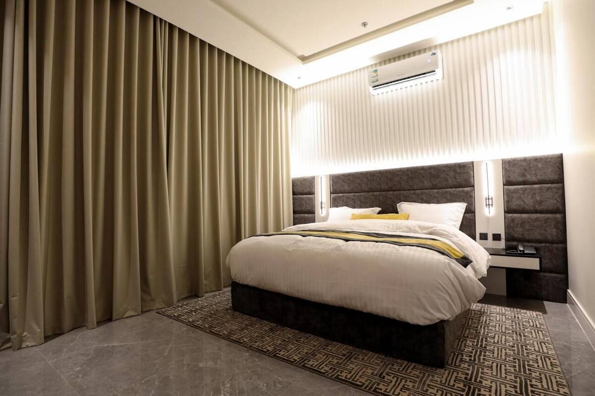 Quarto de hotel moderno com uma cama grande, uma mesa de cabeceira, ar condicionado e um tapete estampado.